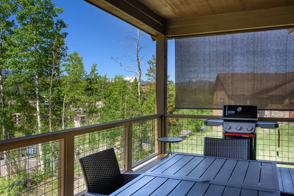 The deck features an outdoor dining table and a gas grill surrounded by leafy trees, offering a relaxing space for barbecues and al fresco dining. The setting is ideal for enjoying mountain air and summer cookouts.