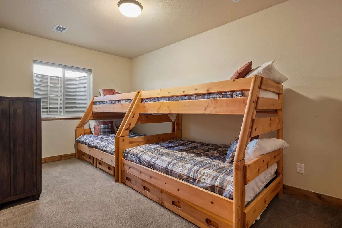 This image features a cheerful bunk room with twin-over-full bunk beds, a wooden dresser, and a window that lets in soft, natural light. The inviting atmosphere suggests a space perfect for children's sleepovers, play, or relaxing with a book or game. The presence of thoughtful details like cozy bedding makes the room both playful and comfortable.