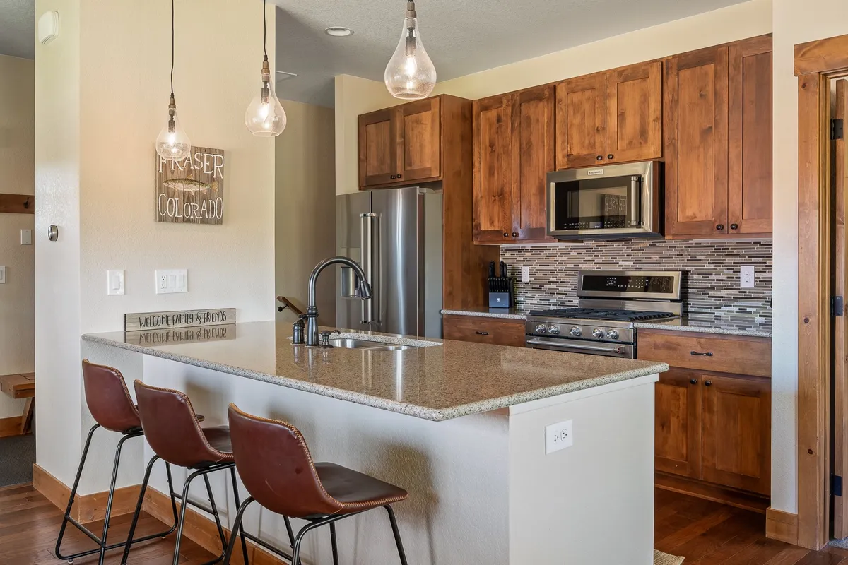 This image features a modern kitchen with granite countertops, pendant lighting, elegant wooden cabinets, and top-of-the-line stainless steel appliances. The open layout and generous workspace are ideal for meal preparation and socializing with guests.