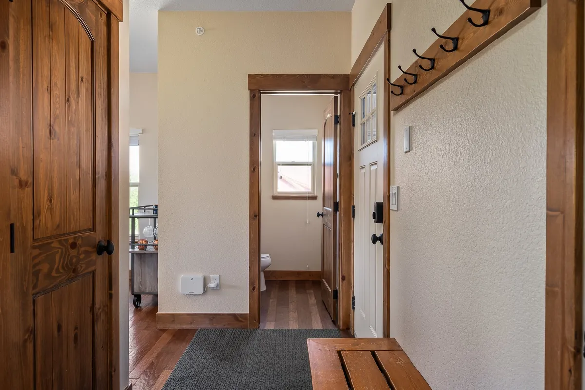 A welcoming mudroom/entryway with a wooden door, entryway bench, and coat hooks. Light-colored walls enhance the inviting, organized atmosphere, ideal for gearing up or winding down after activities.