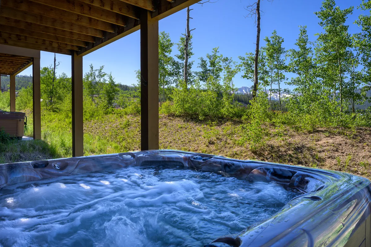 An exterior shot of a private hot tub set amidst greenery with mountains in the background. The scene radiates tranquility and relaxation, inviting guests to unwind while enjoying nature and mountain views.