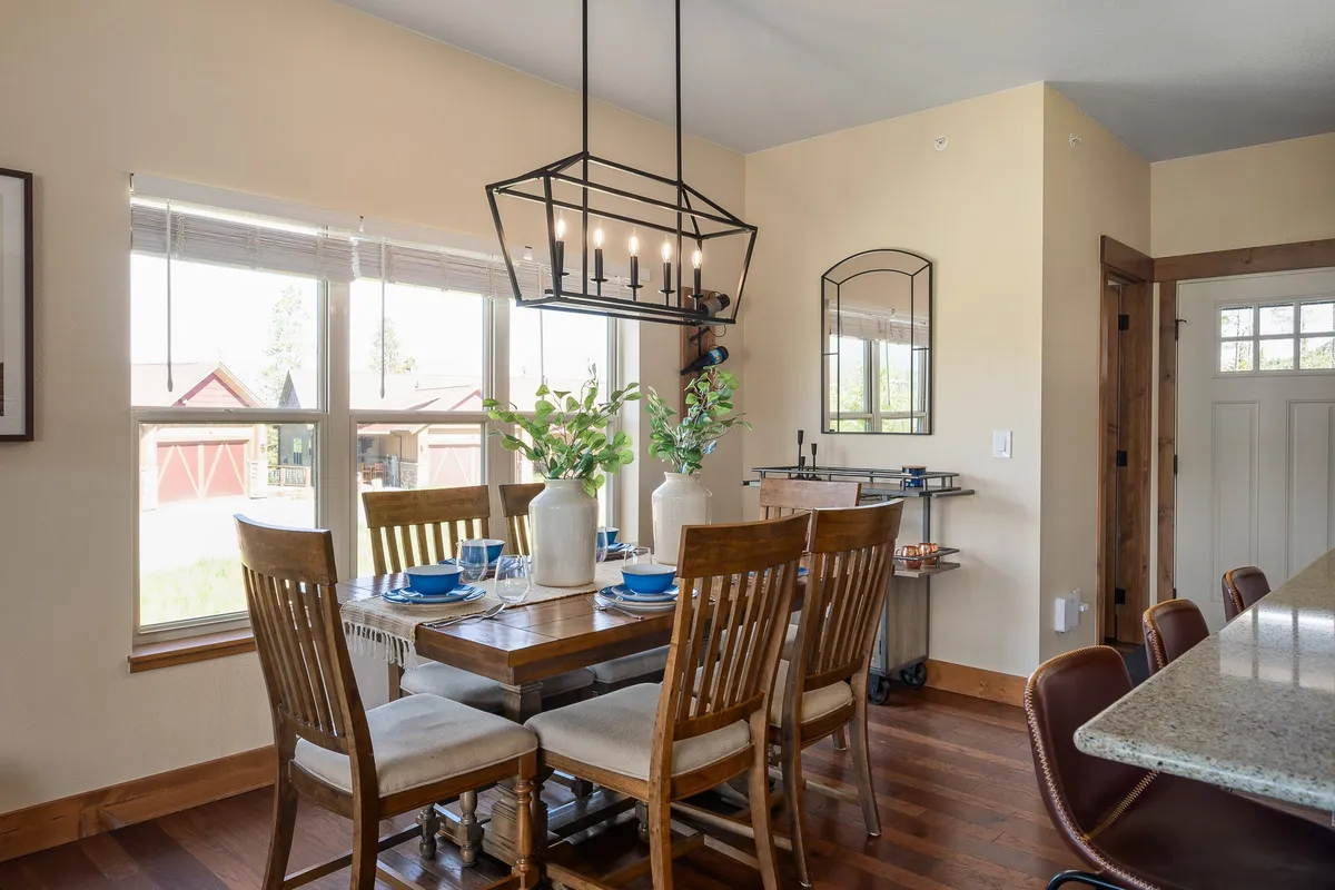 An inviting dining area with a spacious table, elegant light fixture, vase of greenery, and a window offering an inspiring mountain view. The setting is arranged for family dinners or friendly gatherings, capturing the warmth and sociability of shared meals.