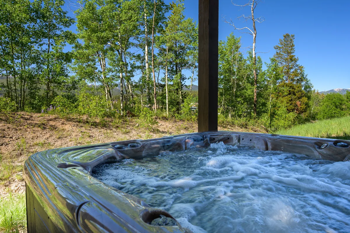 An inviting hot tub nestled on a patio surrounded by trees, offering tranquil mountain views. The scene suggests relaxation after a day of adventure, with the hot tub serving as a prime spot for unwinding outdoors regardless of season.