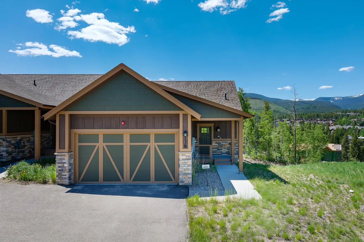 A charming exterior view of the chalet, showcasing the front entrance, garage door, well-maintained landscaping, and stone accents. The setting suggests a spacious, inviting home ideal for group stays, with opportunities for outdoor gatherings and easy access to nearby attractions.