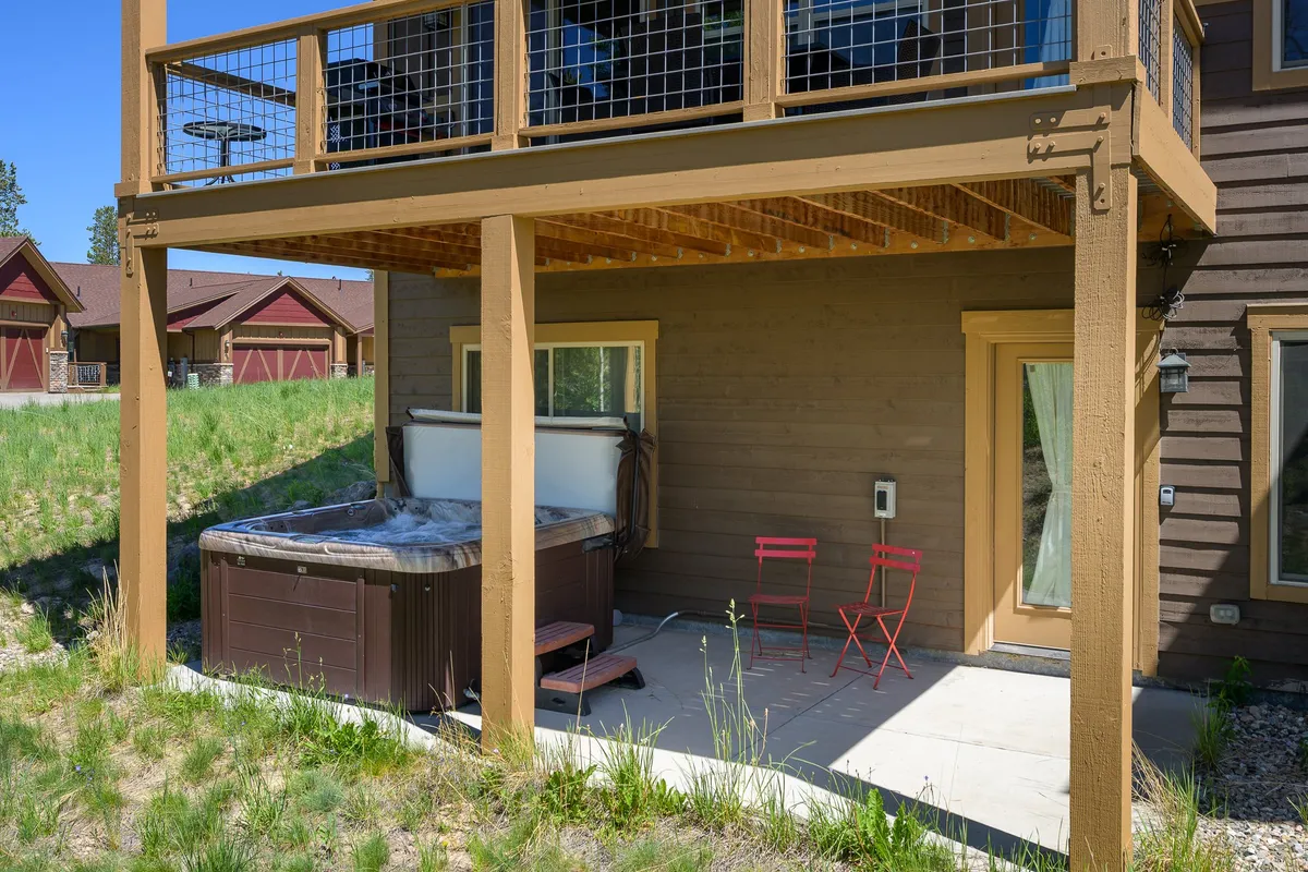 A private patio features a steaming hot tub surrounded by red chairs, inviting guests to unwind while taking in views of the natural landscape. The area feels secluded and tranquil, with ample space for outdoor relaxation and socializing.